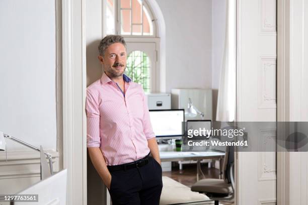 elegant businessman leaning on doorway of office cabin - pink collared shirt stock pictures, royalty-free photos & images