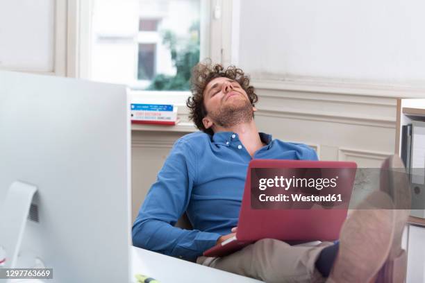 young businessman sleeping with laptop in office cabin - office cabin stockfoto's en -beelden