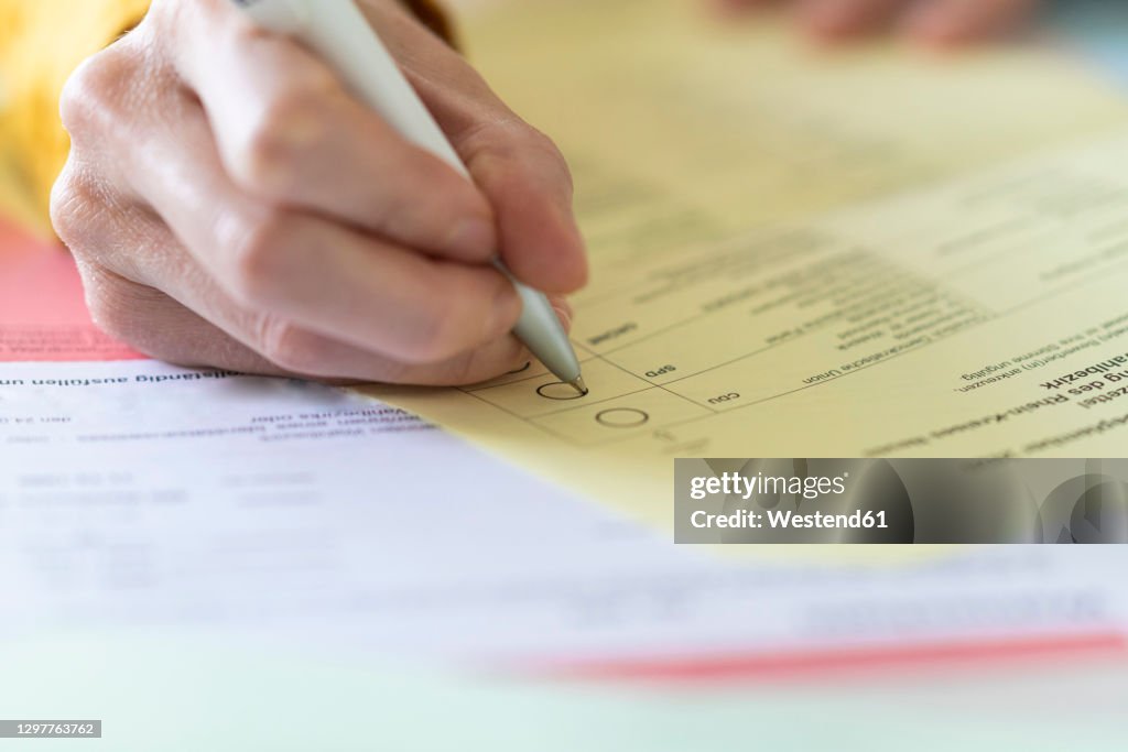 Close-up of woman with pen filling voting form at home