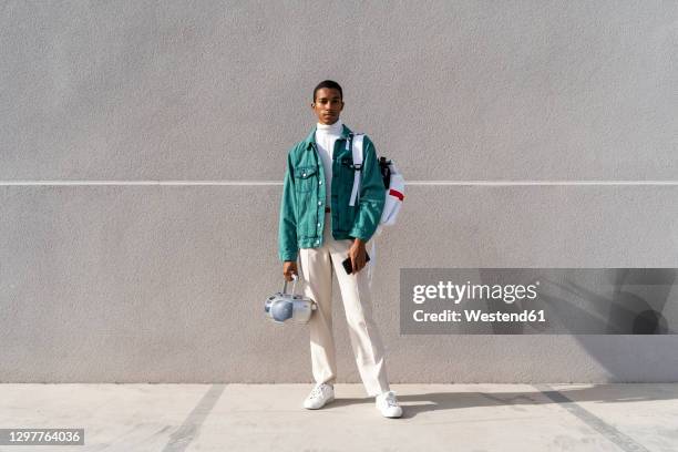 young man with with radio and bag standing against gray wall - mann frontal ganzkörper jacket stock-fotos und bilder