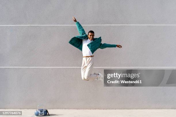 carefree man jumping with arms outstretched against gray wall - gray jacket ストックフォトと画像