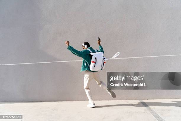 man with backpack and headphones dancing on footpath - ordentlich stock-fotos und bilder