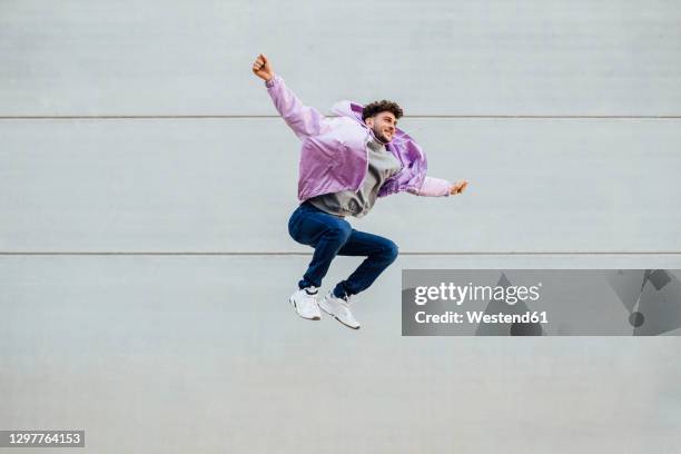 carefree man with arms outstretched jumping against wall - purple jacket fotografías e imágenes de stock