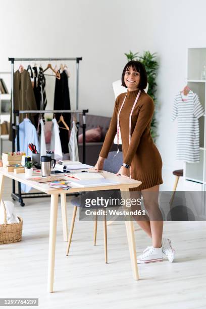 smiling young fashion designer with measuring tape around her neck at atelier - stylist bildbanksfoton och bilder