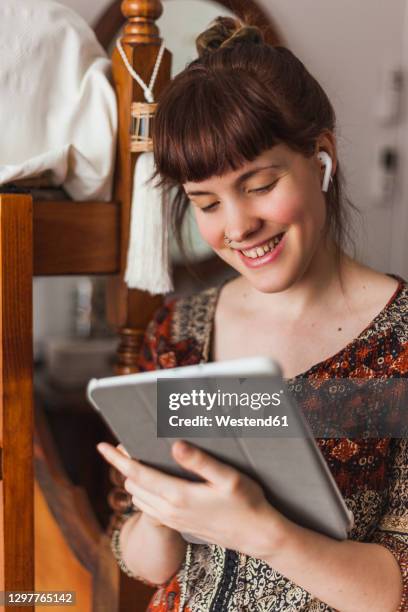 beautiful woman reading news on digital tablet while listening to music through earphones at home - bluetooth imagens e fotografias de stock