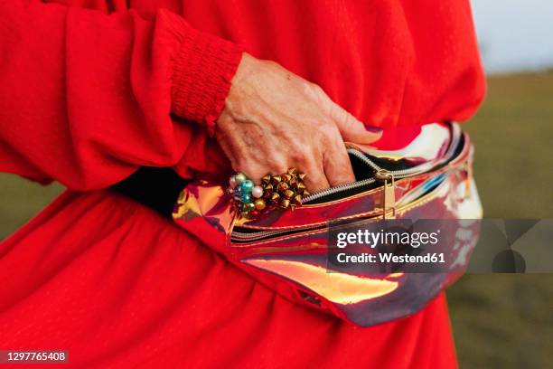 senior woman putting hand in waist pack - bolsa canguro fotografías e imágenes de stock