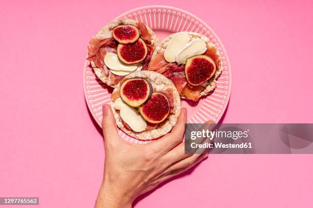 hand of woman picking up rice cake with serrano ham, cheese and fig slices - picking up food stock pictures, royalty-free photos & images