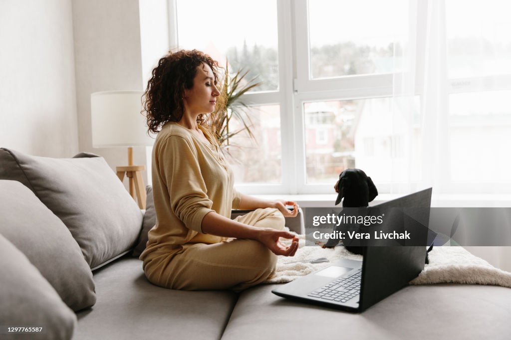 Beautiful smiling woman in Lotus Pose practicing meditation in Living Room at home
