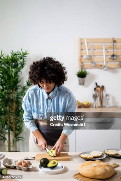 young woman preparing vegan sandwiches in kitchen - cutting avocado stockfoto's en -beelden