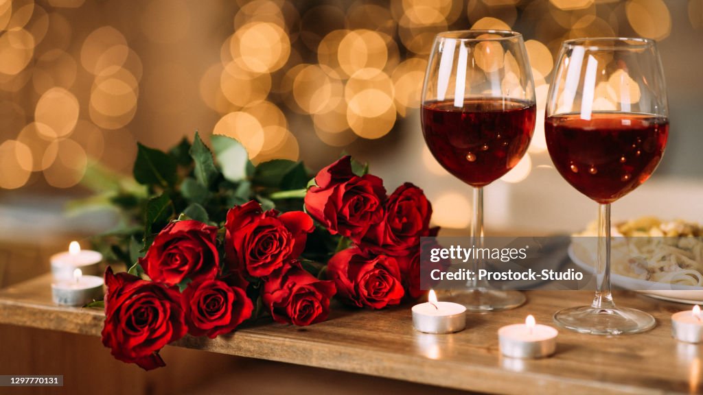 Rosas, dos copas de vino tinto y velas en el escritorio
