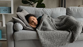 Happy young woman sleeping under blanket on sofa