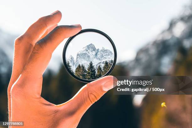 cropped hand holding a camera filter with view of mountain - scherpte stockfoto's en -beelden