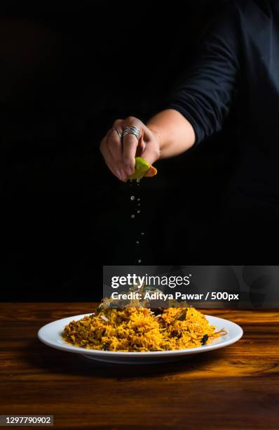 hand of woman squeezing lime juice onto rice dish against black background,pune,maharashtra,india - cuisine indienne photos et images de collection