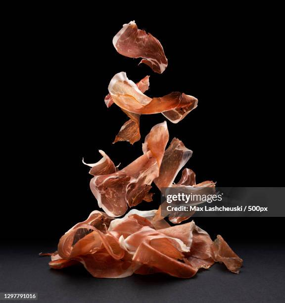 falling ham slices against black background - jambon de parme photos et images de collection