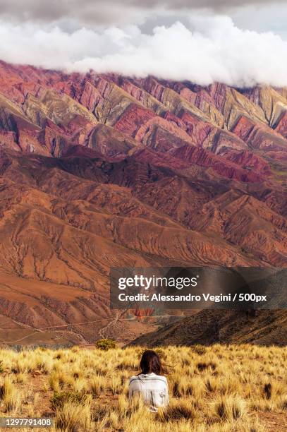 rear view of young woman sitting in front of colorful mountain,jujuy,argentina - provinz jujuy stock-fotos und bilder