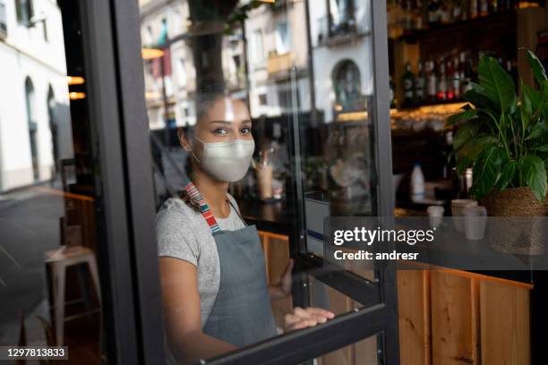 waitress wearing a facemask at a cafe and waiting for clients during the pandemic - overworked waitress stock pictures, royalty-free photos & images