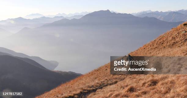 mountainbiker fahren morgens grasbewachsenen bergrücken hinunter - adventure sports stock-fotos und bilder