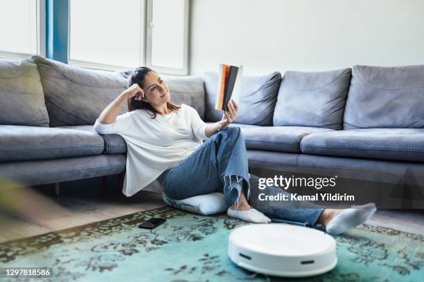 robotic vacuum cleaner cleaning carpet while woman reading a book - vacuum cleaner woman stock pictures, royalty-free photos & images