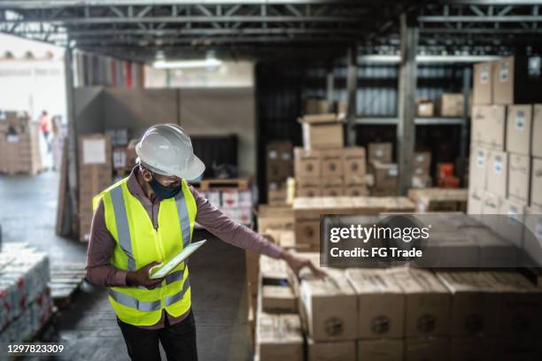 trabajador del almacén que usa máscara facial y productos de comprobación de ropa de trabajo de protección usando tableta digital - cuarto almacén fotografías e imágenes de stock
