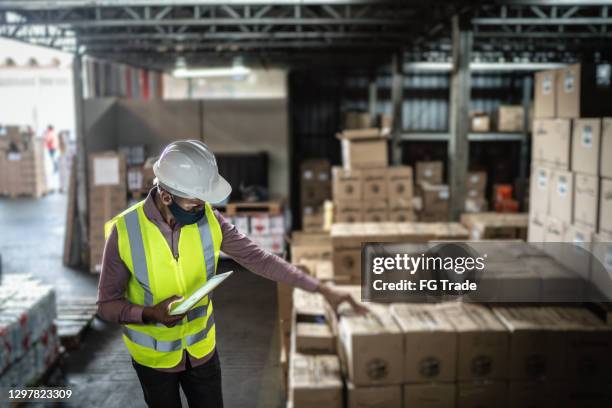 warehouse worker wearing face mask and protective workwear checking products using digital tablet - counting stock pictures, royalty-free photos & images