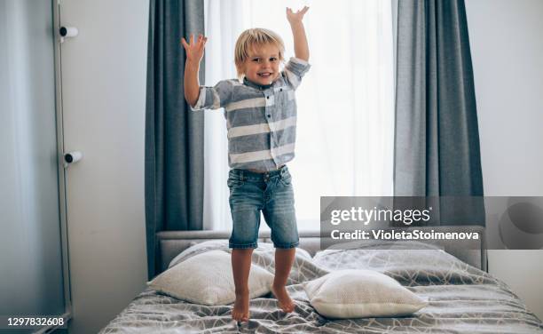 niño saltando sobre la cama. - a boy jumping on a bed fotografías e imágenes de stock