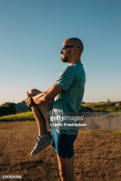 handsome man warming up for an outdoor run by stretching his legs, staying active and fit - standing with hands on knees imagens e fotografias de stock