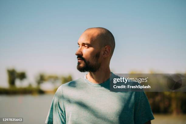 verticale d’un jeune homme dans un t-shirt bleu restant à l’extérieur à côté d’un lac - barbe bleue photos et images de collection