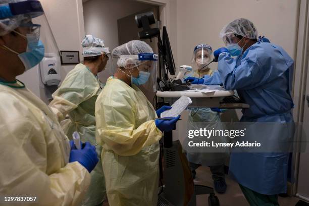 Dr. Renzo Arauco-Brown leads a meeting with his team of medical staff outside of a patient's room while speaking with the pharmacist over the phone...