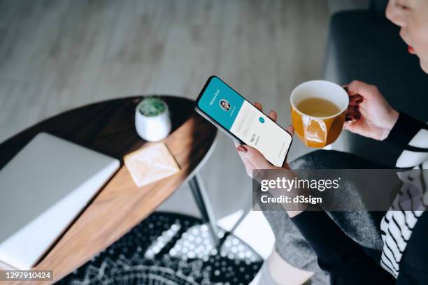 young asian woman relaxing at home drinking a cup of tea, logging in to her smartphone device. lifestyle business, privacy protection, internet and mobile security concept - facebook privacy stock pictures, royalty-free photos & images