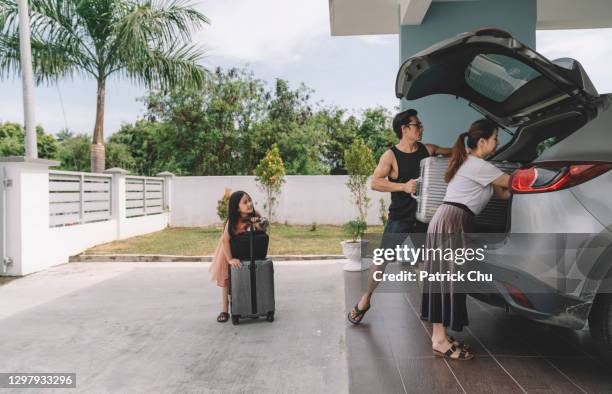 asian chinese couple unloading luggage with their daughter from their car at their house - holiday packing stockfoto's en -beelden