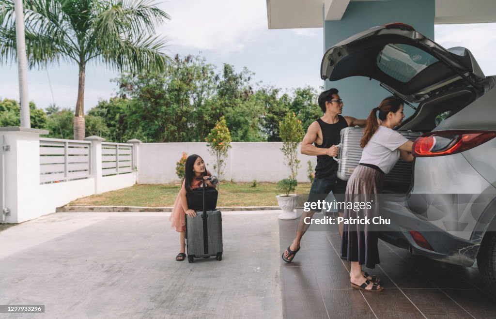 Asian chinese couple unloading luggage with their daughter from their car at their house