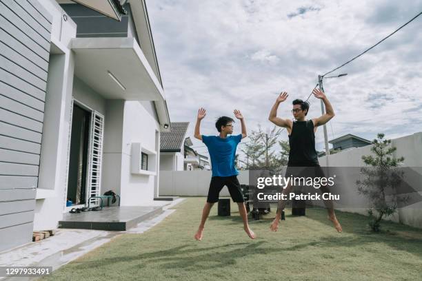 asian chinese teenager and his father doing jumping jacks exercise at backyard of the house - jumping jack stock pictures, royalty-free photos & images