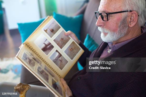 senior mann blick auf die kindheit fotoalbum - witwer stock-fotos und bilder