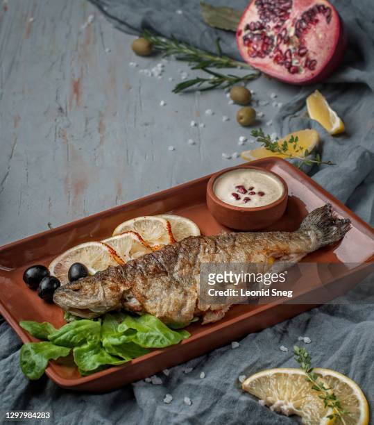 food photography, fried fish side view, served with lemon, herbs and spices on a ceramic brown dish, on gray textured background close up - goldbrasse stock-fotos und bilder