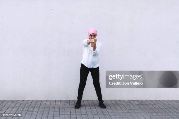 woman in the centre of the image, she is looking forward and is with her right arm stretched and with both fists clenched as a sign of struggle and is wearing a pink scarf in reference to cancer, she is wearing black pants and a white blouse. - best bosom fotografías e imágenes de stock