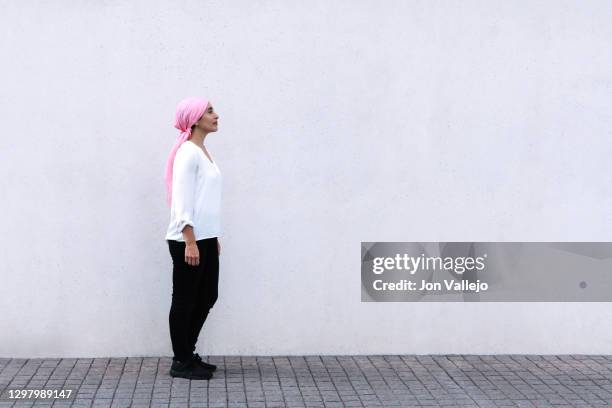 woman to the left of the image and looking up with a pink scarf in reference to cancer, is wearing black pants and a white blouse. - ribbon in mouth stock pictures, royalty-free photos & images