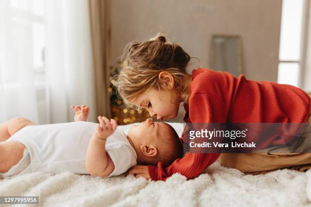 adorable child kissing little sister lying on white bedding - sibling stock pictures, royalty-free photos & images