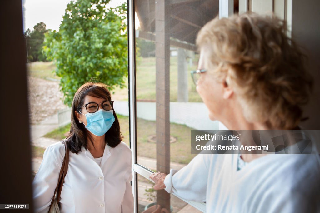 Mujer mayor que abre la puerta para la enfermera en el hogar de la atención médica