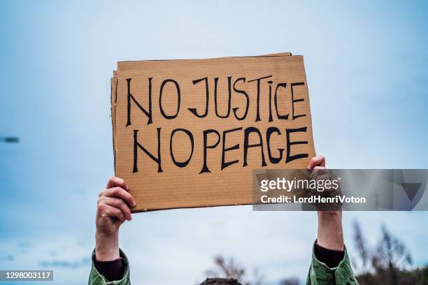 man hand holding placard with text "no justice no peace" - placard stock pictures, royalty-free photos & images