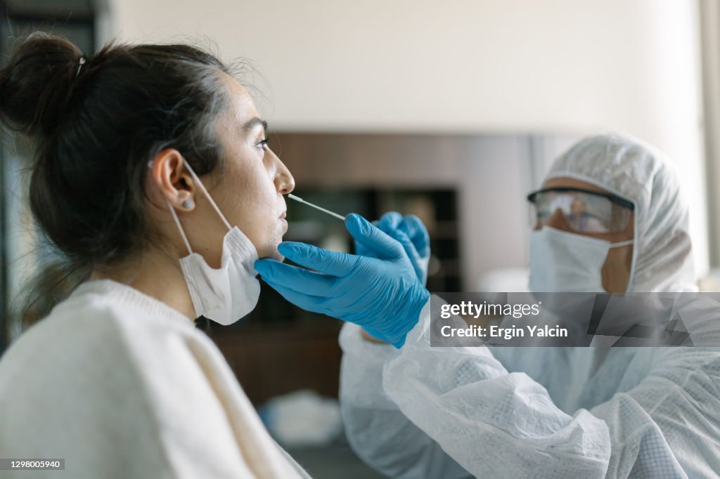 Doctor in protective workwear taking nose swab test from young woman