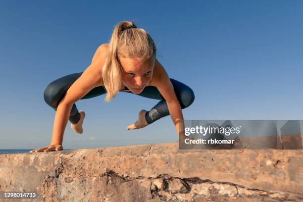 young teenage girl in sportswear doing a difficult handstand by the sea - girl yoga stock pictures, royalty-free photos & images