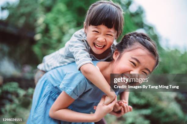 lovely girl carrying her little sister on back in park - asia kid stockfoto's en -beelden