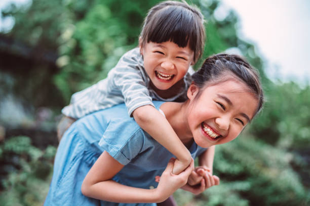 lovely girl carrying her little sister on back in park - happy kids stock pictures, royalty-free photos & images