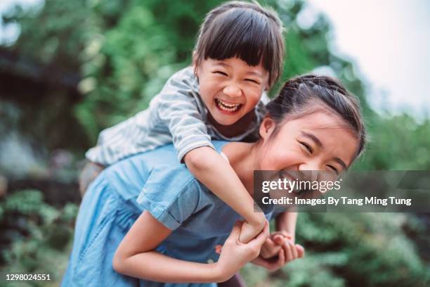 lovely girl carrying her little sister on back in park - sister stock pictures, royalty-free photos & images