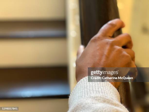 african-american woman grips handrail as she climbs stairs at home - railing stockfoto's en -beelden