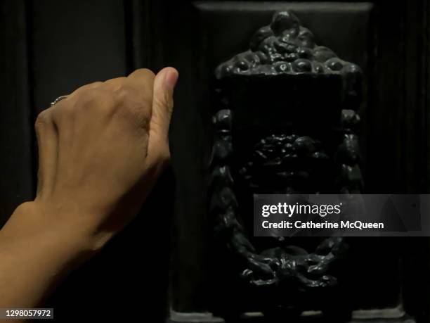 african-american woman knocks on front door of a home at night - knocking stockfoto's en -beelden