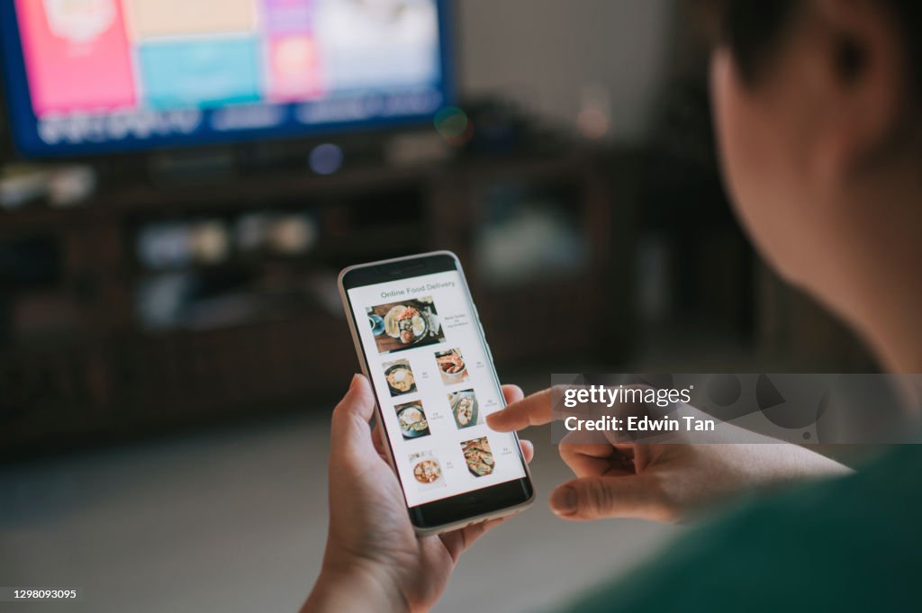 Online-Lebensmittellieferung mobile App auf Smartphone-Bildschirm von asiatischen Frau Hände im Wohnzimmer gezeigt