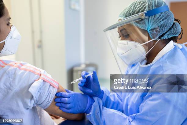 doctor in personal protective equipment vaccinating a patient - covid 19 vaccine stock pictures, royalty-free photos & images