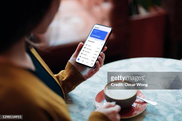 close-up shot of young woman managing bank account on smartphone at cafe - account money lifestyle stock-fotos und bilder