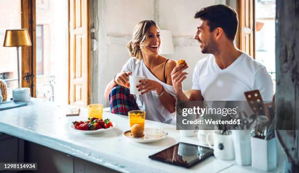 happy young couple sitting at table and having breakfast at home - muffin stockfoto's en -beelden
